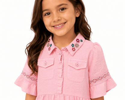 Young girl wearing a pink dress with floral embroidery on a white background